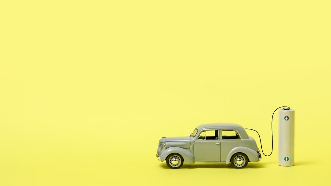 a-gray-toy-car-and-a-battery-on-a-yellow-backgroun-2022-11-09-04-37-19-utc